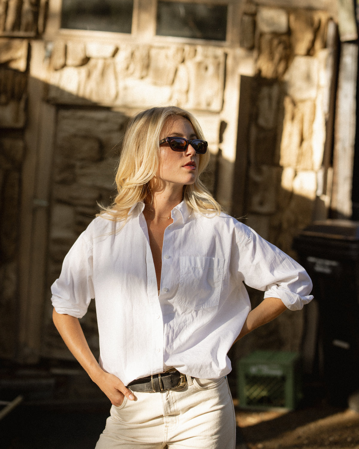 Woman in a white button-up shirt wearing black ETC sunglasses outside a rustic wooden building