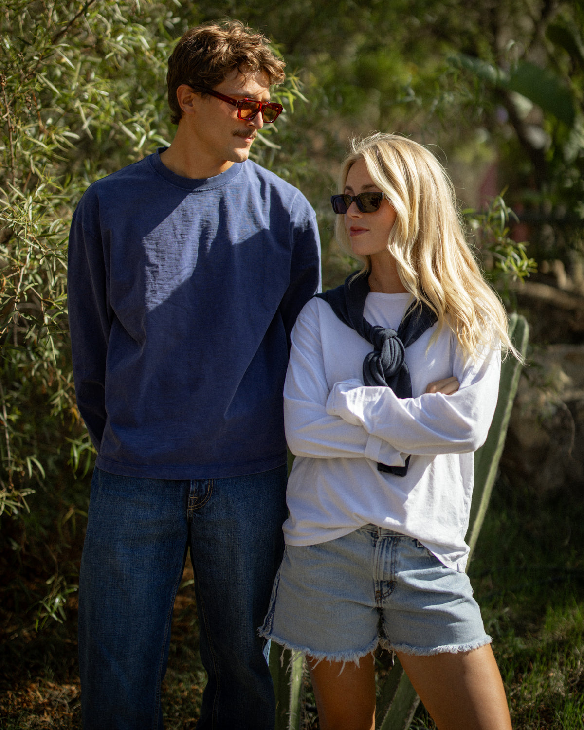 Man in a navy sweater and woman in a white top and denim shorts, both wearing ETC sunglasses outdoors