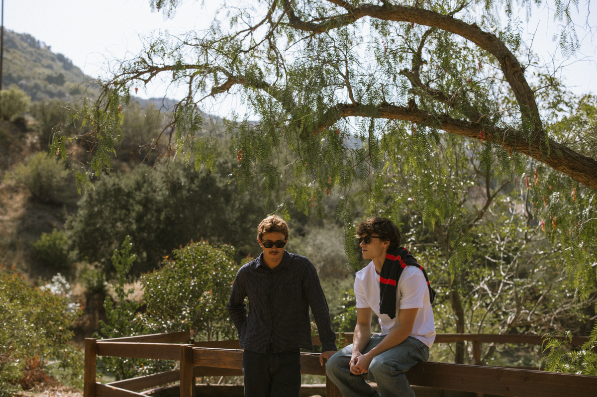 Two people in ETC sunglasses sitting on a wooden bench under an oak tree in the hills